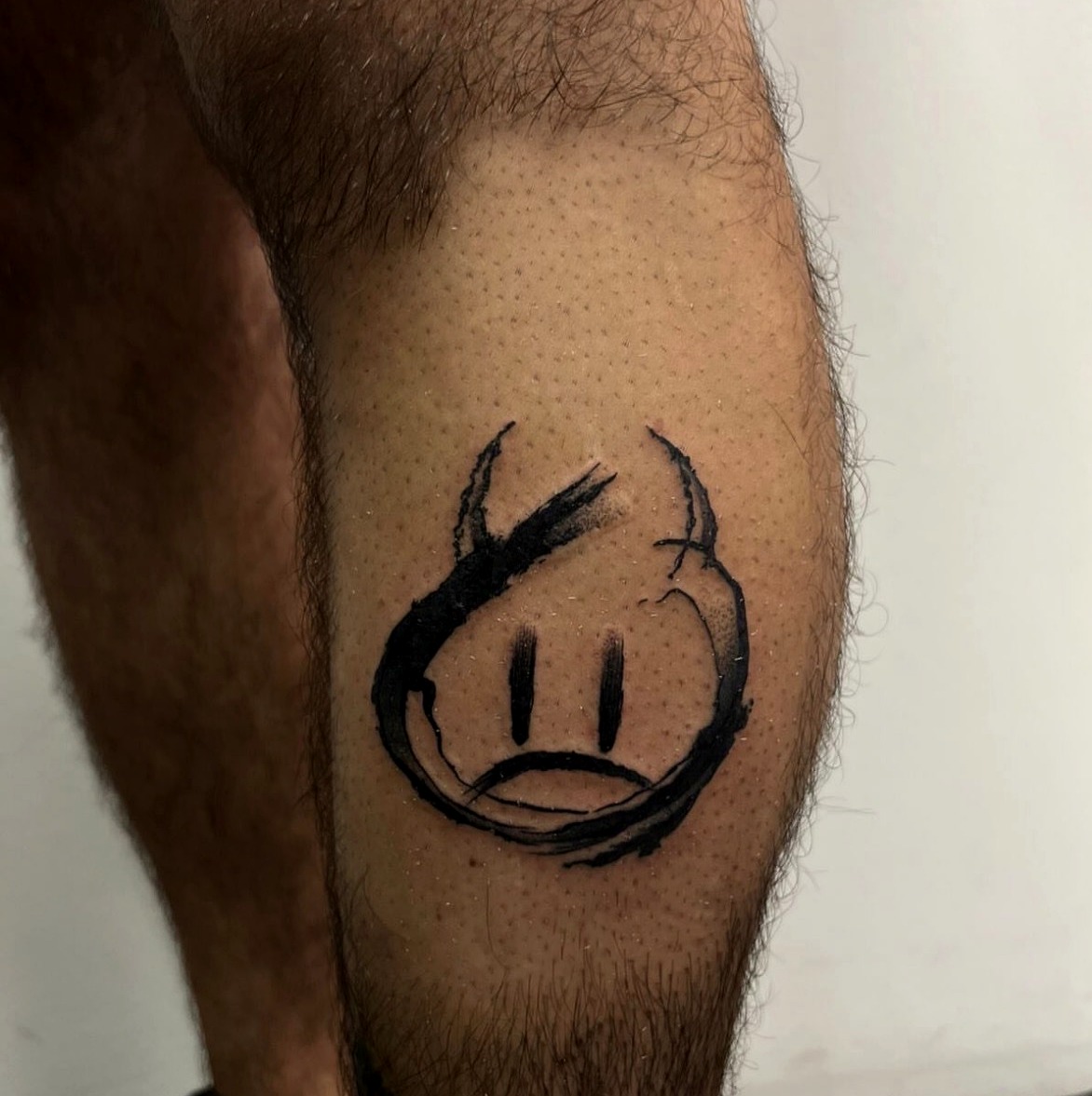 Bold brushstroke sad face tattoo on the calf
